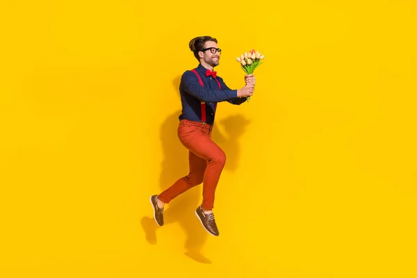Full size profile side photo of young guy jump up hold bunch of tulips present look empty space isolated over yellow color background — Stock Photo, Image