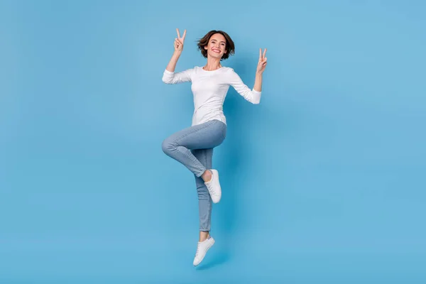 Pełny rozmiar zdjęcie podekscytowany szalony pozytywna dziewczyna skacze w górę wygłupiając się wokół pokazać v-znak izolowany na tle niebieskiego koloru — Zdjęcie stockowe