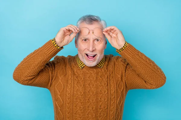 Φωτογραφία του εντυπωσιασμένος ενθουσιασμένος συνταξιούχος φορούν καφέ γυαλιά βραχίονα πουλόβερ ανοιχτό στόμα απομονωμένο φόντο μπλε χρώμα — Φωτογραφία Αρχείου