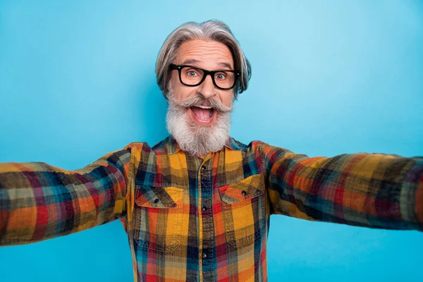 Foto de impressionado homem aposentado funky desgaste xadrez camisa óculos tacking selfie boca aberta isolado azul cor fundo — Fotografia de Stock
