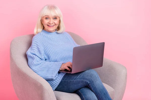 Портрет привлекательной веселой седой женщины с помощью ноутбука, смотрящей фильм на розовом пастельном фоне — стоковое фото