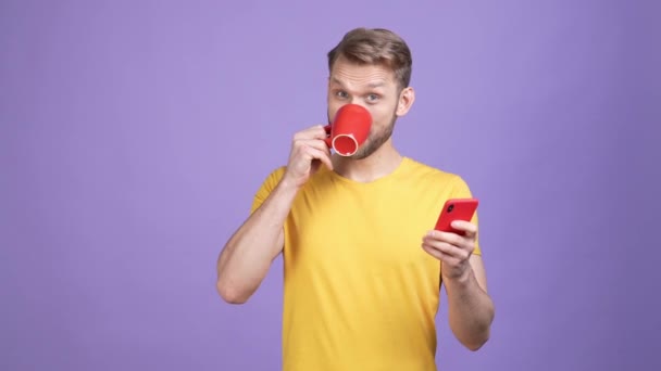 Millennial cara beber caneca bebida uso dispositivo isolado cor roxa fundo — Vídeo de Stock