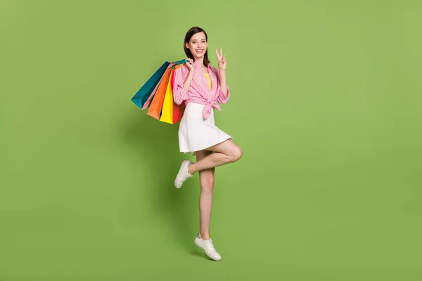 Full size photo of smiling female go shopping showing v-sign gesture relaxing isolated on green color background — Stock Photo, Image