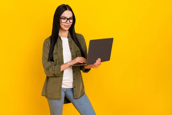 Bild av vacker tusenårig dam titta bärbar dator bära glasögon khaki skjorta jeans isolerad på gul bakgrund — Stockfoto