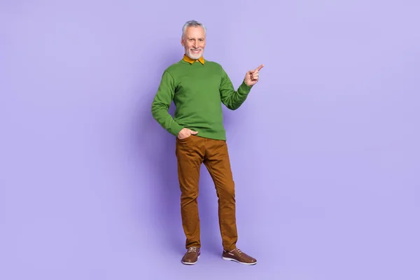 Фото очаровательного пенсионера, одетого в зеленый пуловер, указывающий на пустое пространство изолированного фиолетового цвета фона — стоковое фото