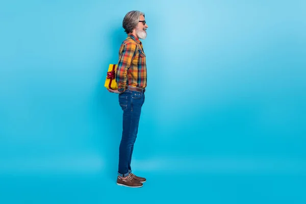 Foto de hombre jubilado divertido excitado usar gafas de camisa a cuadros ocultando la caja actual aislado fondo de color azul —  Fotos de Stock