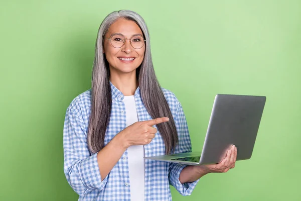 Фото милой пожилой дамы с белой прической показывает, что ноутбук носить голубую рубашку изолированы на зеленом фоне — стоковое фото