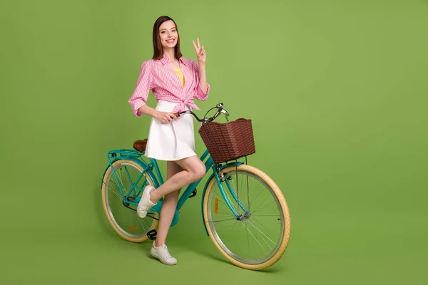 Pełny rozmiar zdjęcie marzycielski pozytywna dziewczyna jazda na rowerze pokazując v-znak podróży izolowane na zielonym tle — Zdjęcie stockowe