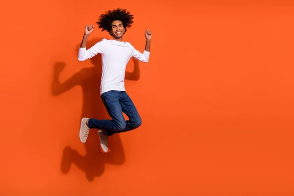 Foto de tipo encantador afortunado usar camisa blanca saltando puños altos espacio vacío aislado color naranja fondo —  Fotos de Stock