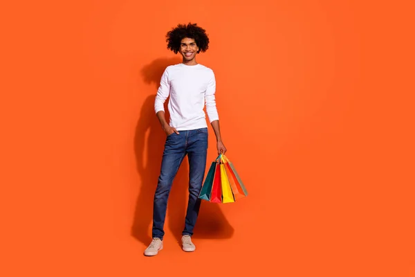 Φωτογραφία του γοητευτικό ελκυστική τύπος ντυμένος λευκό πουκάμισο κρατώντας αγοραστές περπάτημα κενό χώρο απομονωμένο φόντο πορτοκαλί χρώμα — Φωτογραφία Αρχείου