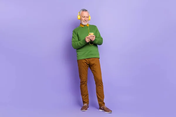 Foto de homem aposentado muito bonito usar camisola verde apreciando músicas moderno dispositivo isolado cor violeta fundo — Fotografia de Stock