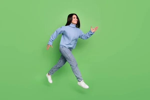 Foto de senhora bonita adorável vestido suéter azul levantando punhos saltando alto correndo rápido isolado cor verde fundo — Fotografia de Stock