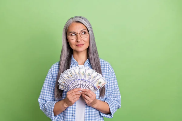 Foto di bello invecchiato capelli bianchi signora tenere i soldi sguardo promo usura occhiali camicia a scacchi isolato su sfondo di colore verde — Foto Stock