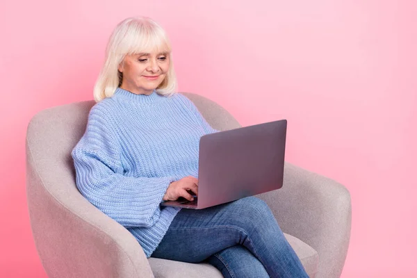 Портрет привлекательной сфокусированной седой женщины с помощью ноутбука, пишущей электронную почту на розовом пастельном фоне — стоковое фото