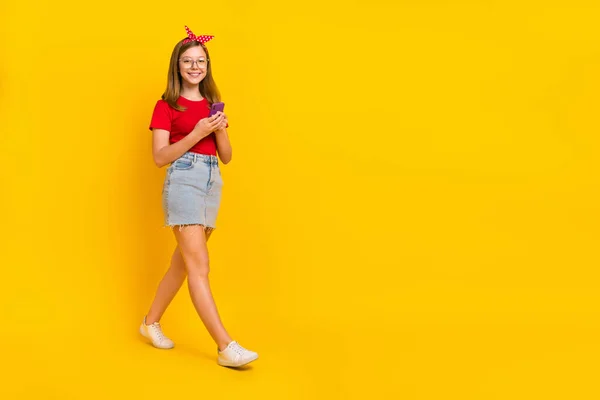 Foto em tamanho completo de adorável encantador menina criança ir a pé com telefone pouco influenciador adolescente isolado no fundo de cor amarela — Fotografia de Stock