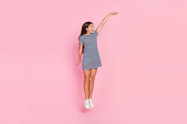 Foto van charmante opgewonden meisje dragen gestreepte jurk springen hoog meten lege ruimte geïsoleerde roze kleur achtergrond — Stockfoto