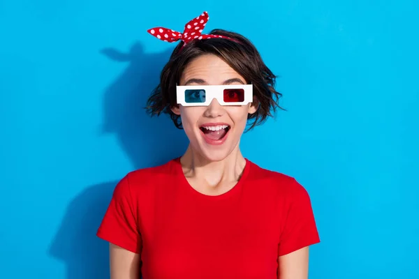 Bild av imponerad ung brunett dam titta på tv bära röd t-shirt pannband glasögon isolerad på blå färg bakgrund — Stockfoto