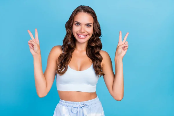 Foto indah berambut cokelat keriting gaya rambut wanita menunjukkan v-sign memakai singlet teal terisolasi di latar belakang warna biru — Stok Foto