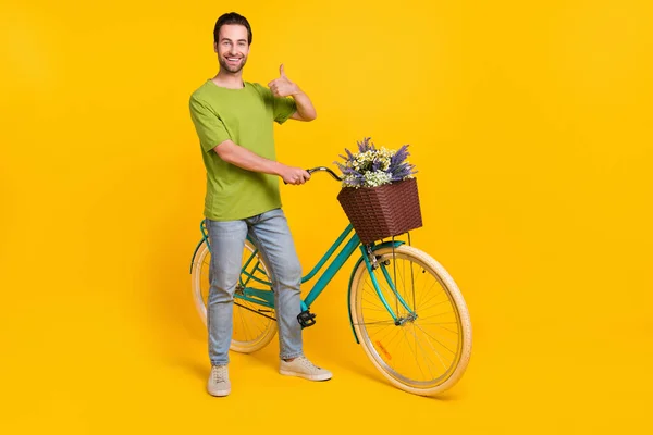 Фотографія повного тіла крутого брюнетки зачіски тисячоліття хлопець показує великий палець на велосипеді носити футболки джинси взуття ізольовані на жовтому тлі — стокове фото