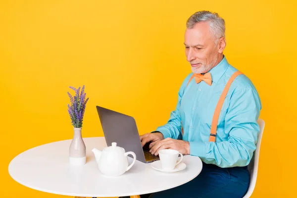 Photo de drôle homme à la retraite mignon porter des bretelles chemise turquoise assis cafe bavardage dispositif isolé couleur jaune fond — Photo