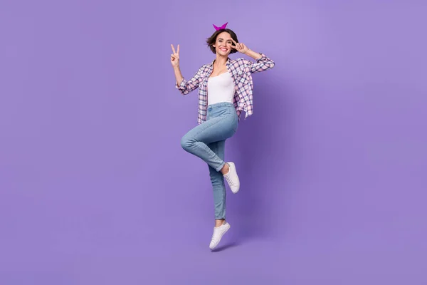 Zdjęcie uroczej uroczej kobiety nosić koszulę w kratę skacząc wysoki v-znak okładka oko odizolowane fioletowy kolor tła — Zdjęcie stockowe