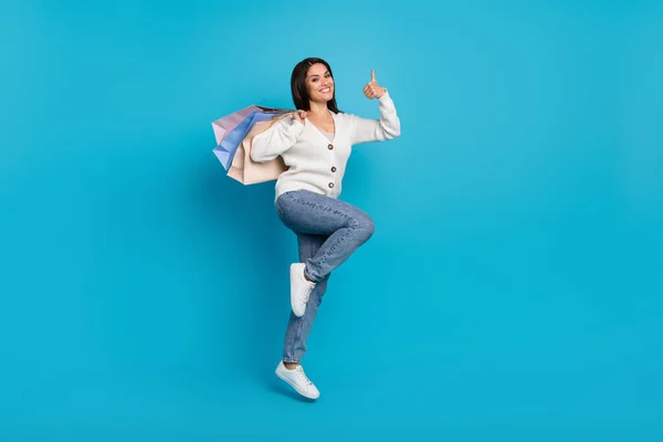 Foto van schattige glanzende dame gekleed wit vest dragen shoppers springen hoge duim omhoog geïsoleerde blauwe kleur achtergrond — Stockfoto