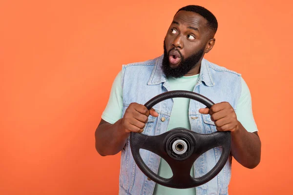 Photo of impressed afro guy wear denim vest driving car looking empty space isolated orange color background — Stock Photo, Image