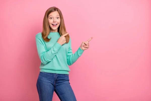 Foto de excitada chica de la escuela funky vestido jersey verde azulado apuntando espacio vacío aislado color rosa fondo — Foto de Stock