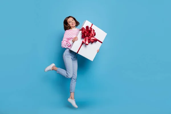 Full body photo of cute millennial lady jump with present wear shirt jeans shoes isolated on blue background