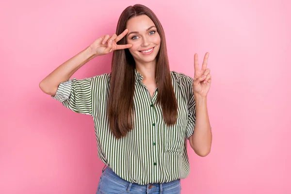 Foto de linda mujer divertida usar camisa a rayas sonriendo mostrando v-signo de la cubierta del ojo aislado de color rosa fondo —  Fotos de Stock