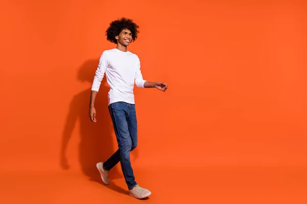 Foto de chico bastante encantador vestido camisa blanca caminando buscando espacio vacío aislado color naranja fondo — Foto de Stock