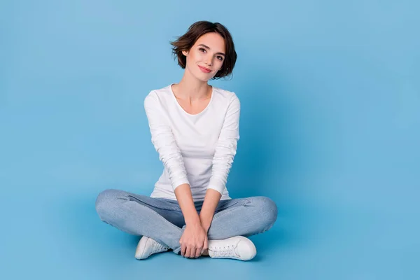 Foto de linda mujer bonita usar camisa blanca sentado piernas cruzadas espacio vacío aislado color azul fondo — Foto de Stock