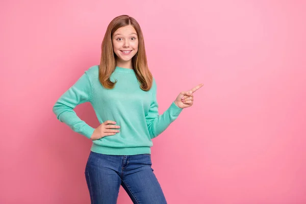 Foto de linda colegiala encantadora usar suéter turquesa apuntando espacio vacío aislado color rosa fondo —  Fotos de Stock