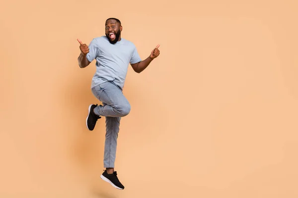 Volledige lichaamsomvang uitzicht van aantrekkelijke vrolijke koele man springen tonen thumbup geïsoleerd over beige pastel kleur achtergrond — Stockfoto