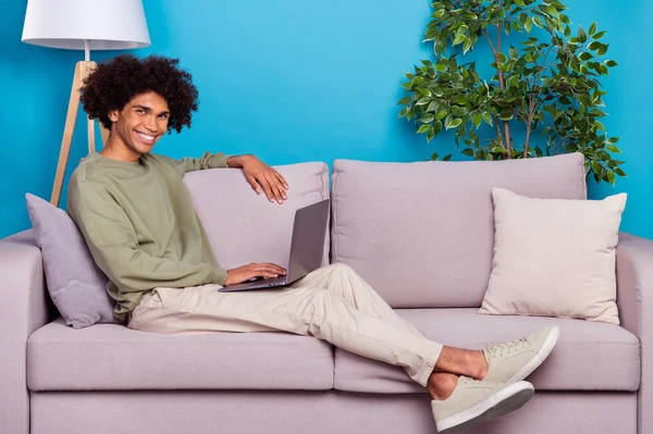 Full size profil boční fotografie mladého chlapa sedět gauč víkend odpočinek pohodlí použít notebook izolované přes modré barvy pozadí — Stock fotografie