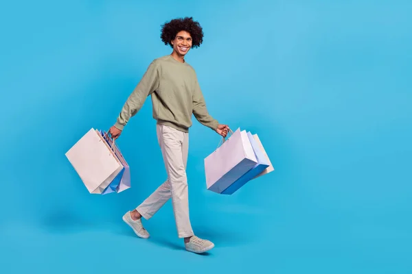 Full size profiel zijkant foto van jonge man lopen hold winkeltassen winkel korting geïsoleerd over blauwe kleur achtergrond — Stockfoto