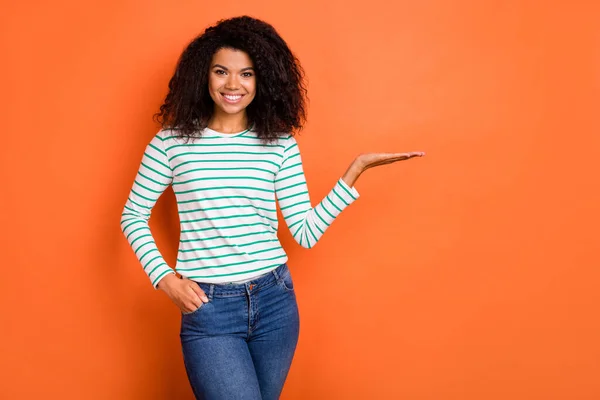 Photo of optimistic young wavy hairdo lady hold empty space wear white shirt isolated on orange color background — Stock Photo, Image