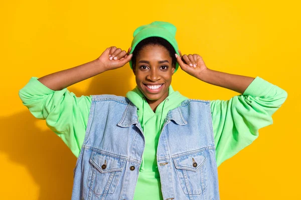 Porträtt av attraktiv glad flicka vidröra fastställande huvudbonader isolerad över ljusa gula färg bakgrund — Stockfoto