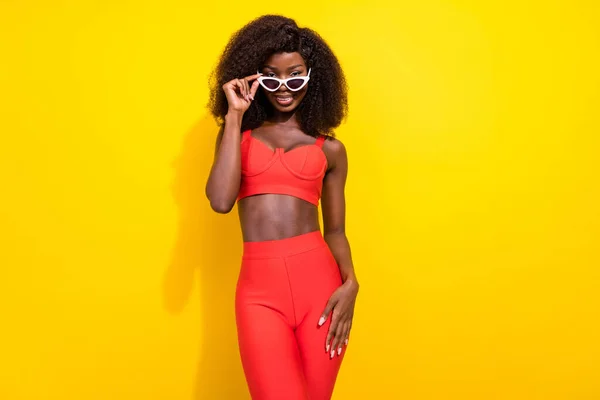 Фото солодкої впевненої африканки, одягненої в червоний сексуальний одяг рука темних окулярів посміхається ізольований жовтий колір фону — стокове фото