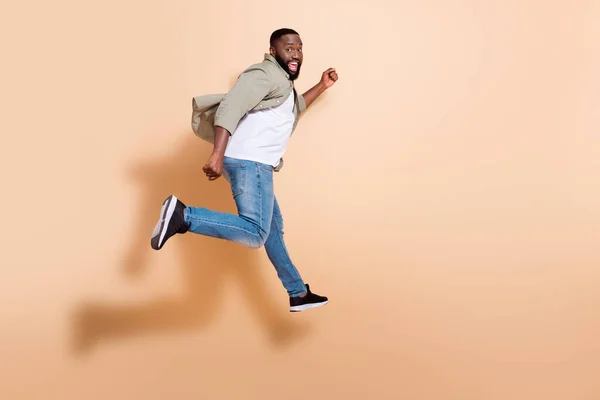 Volledige profiel foto van grappige jonge baard guy run wear shirt jeans sneakers geïsoleerd op beige achtergrond — Stockfoto