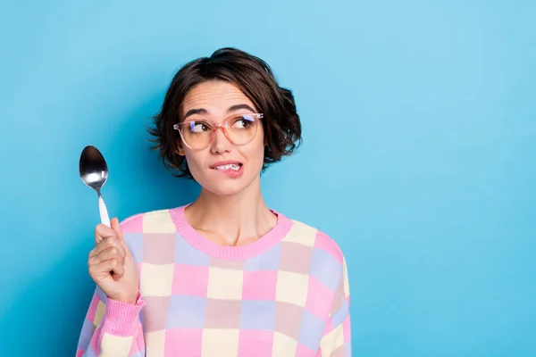 Foto van schattige duizendjarige brunette dame houden lepel kijken ad slijtage bril geruite trui geïsoleerd op blauwe achtergrond — Stockfoto