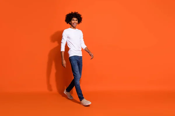 Foto de cara doce atraente usar camisa branca andando espaço vazio isolado cor de fundo laranja — Fotografia de Stock