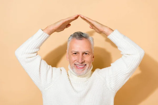 Portrait of attractive cheerful safe grey-haired man showing roof over head new life isolated over beige pastel color background — Stock Photo, Image