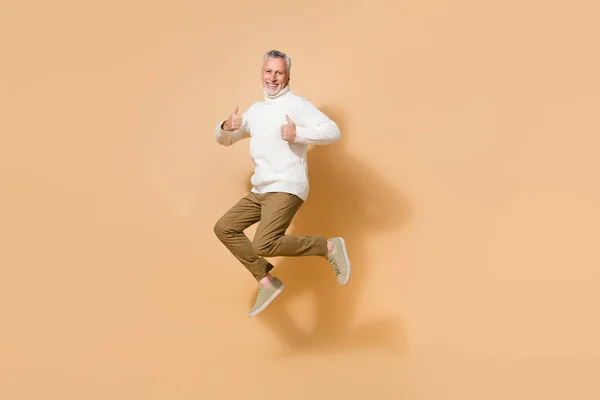 Full length body size view of attractive cheerful lucky man jumping showing thumbup isolated on beige pastel color background — Stock Photo, Image