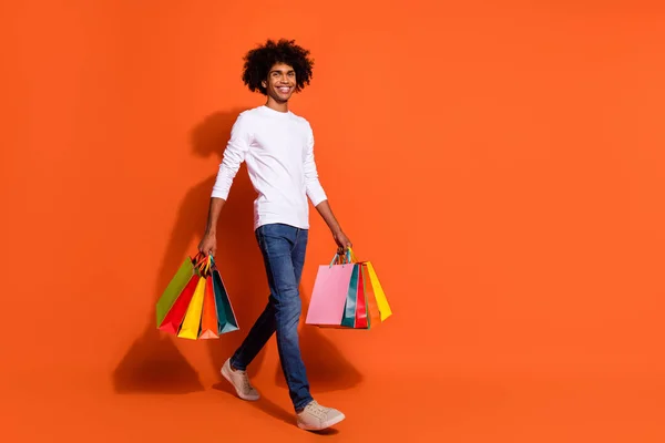 Foto von attraktiven hübschen Kerl gekleidet weißes Hemd tragen Käufer zu Fuß leeren Raum isoliert orange Farbhintergrund — Stockfoto