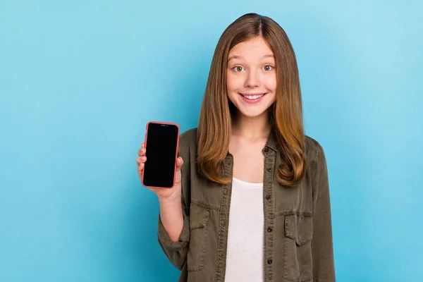 Photo de positive mignonne petite fille tenir le téléphone recommander la promotion du nouveau produit isolé sur fond de couleur bleue — Photo