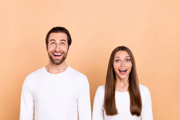 Portret van aantrekkelijke vrolijke verbaasd trendy bruinharige echtgenoten opzoeken kopieerruimte wow geïsoleerd over beige pastel kleur achtergrond — Stockfoto
