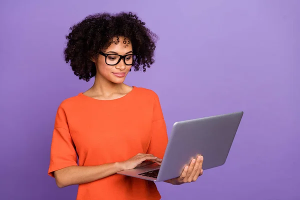 Foto de inteligente jovem senhora tipo laptop desgaste laranja t-shirt isolado no fundo cor violeta — Fotografia de Stock
