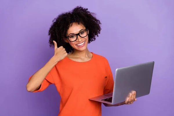 Zdjęcie funky tysiąclecia brunetka pani trzymać laptop kciuk do góry nosić okulary pomarańczowy t-shirt izolowany na fioletowym tle — Zdjęcie stockowe