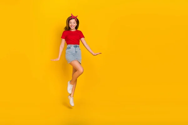 Foto de corpo inteiro de cool menina pequena salto desgaste t-shirt hairband jeans saia sapatos isolados no fundo amarelo — Fotografia de Stock